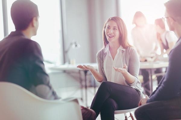 A woman being interviewed by two men in a sunlit open plan office.