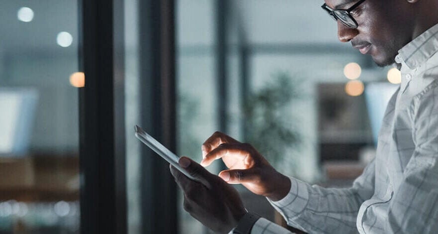 Male dressed in corporate attire holding a laptop in a glass office