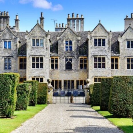 A large mansion and country estate where a house manager works. It is sunny and there is a beautiful driveway and hedges.