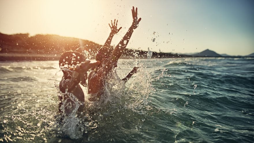 Children and an adult playing in the sea at sunset