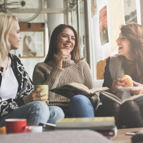 Three girls learning and eating in a cafe with books, coffees and snacks while sitting on a couch.