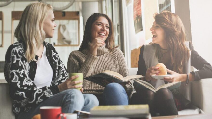 Three girls learning and eating in a cafe with books, coffees and snacks while sitting on a couch.
