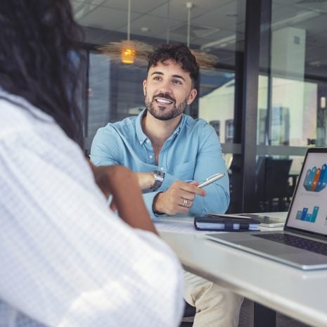A man and woman talking in an office over a laptop showing graphs.