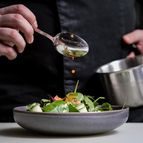 Close-up of a chef holding a spoon and finishing a dish.
