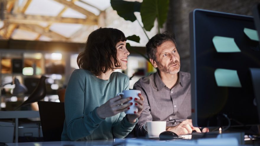 Colleagues sitting together at a computer, observing the content of the screen.