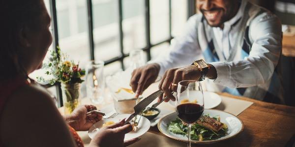 A lifestyle manager has dinner with a colleague in a fine dining restaurant with two delicious dishes and glasses of wine.
