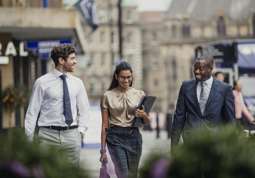 Three business people walking and talking on a city street.