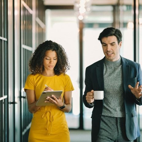 An assistant taking notes as she walks through an office with her manager.
