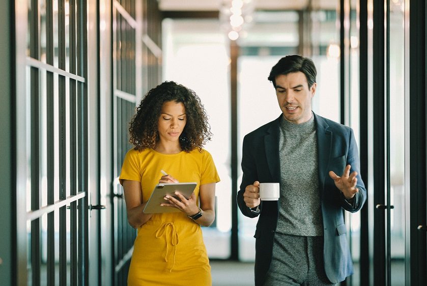 An assistant taking notes while talking with their manager in an office.