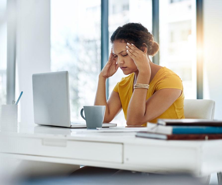 A business woman holding her head while closing her eyes, feeling stressed and anxious at her workplace.