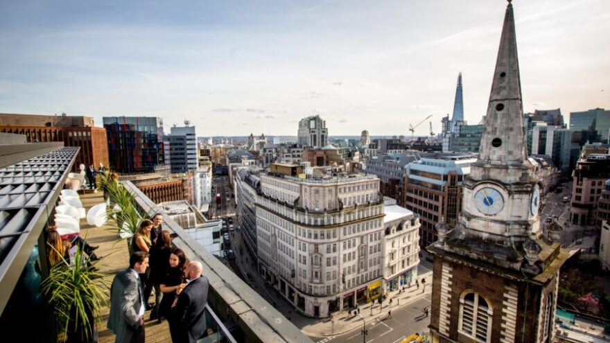 Rooftop cocktail bar with people drinking in the sun, view of the Gherkin and other buildings in down town London