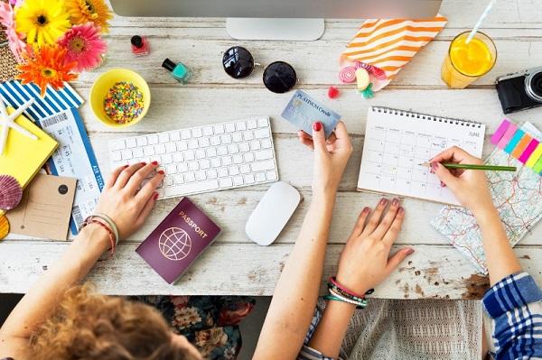 Two PAs buying plane tickets on a computer, with a passport, credit card and planning an itinerary.