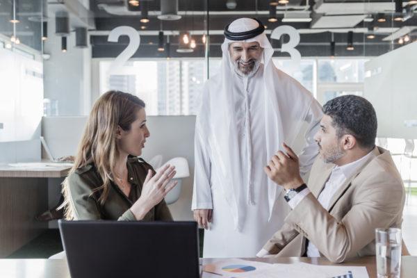 Business people discussing global business in modern office, mature Arab businessman wearing traditional clothing