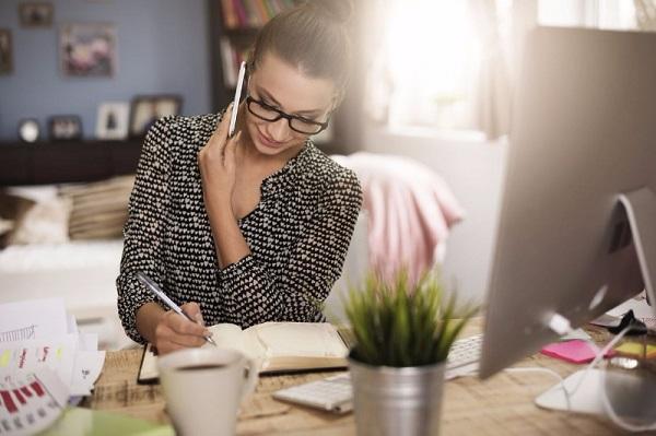 A private PA sits at her desk on the phone while writing something down in a notepad.