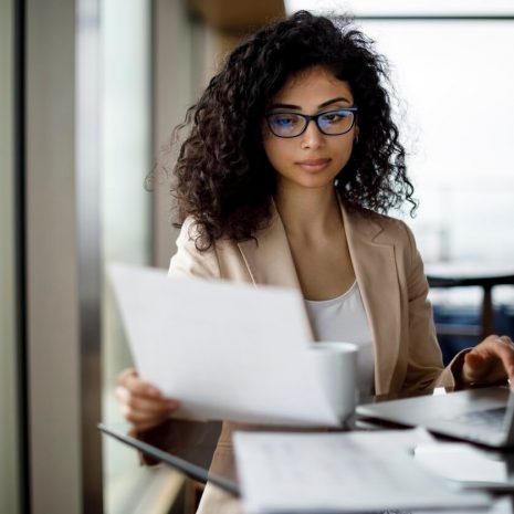 Woman looking at notes and typing on laptop in an office.