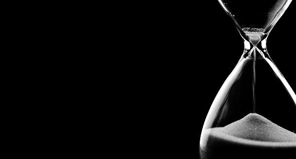 A black background with an hourglass in the foreground, with white sand dropping into the bottom part.
