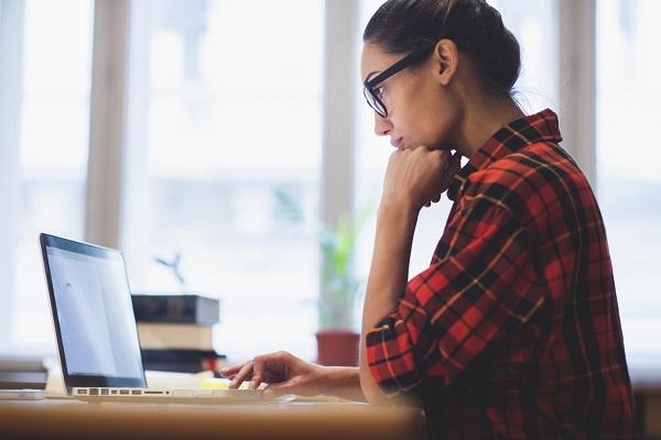 A woman sitting at a bench with her laptop researching a company’s background before she attends an interview.