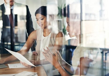 A small human resources team of three people in a creative office with glass walls are having a strategy meeting together.