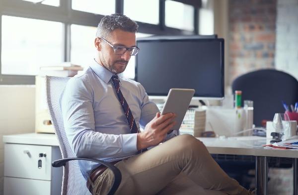 A smart business man sits at his desk with an iPad.