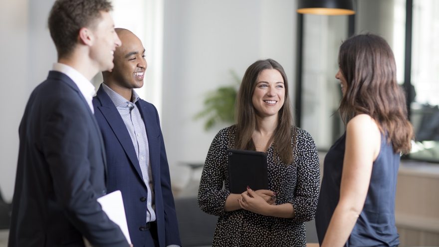 A group of colleagues smiling and talking in an office.