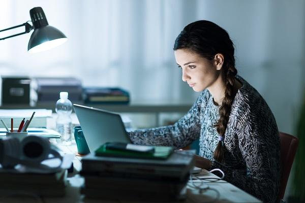 A woman sitting at work writing a cover letter after hours when everyone else has gone home.