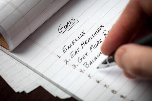 A person writes a list of goals including exercise, eating healthier, getting more rest and staying productive at work.