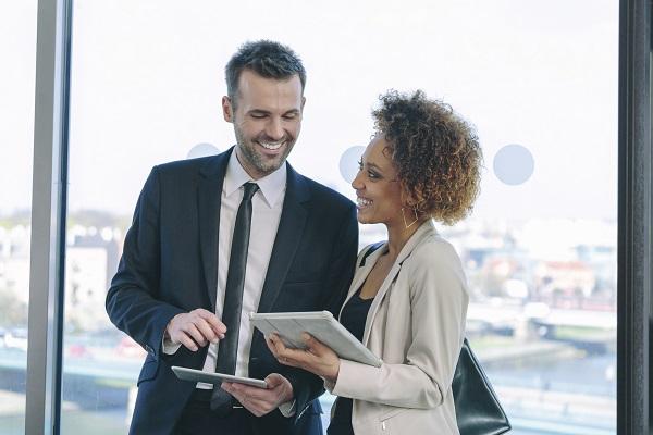 Two recruitment consultants using an iPad and smiling by a window.