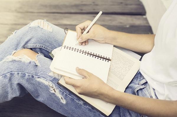 A woman holding a book and a notebook in her lap. She’s writing notes and constructing a successful CV.