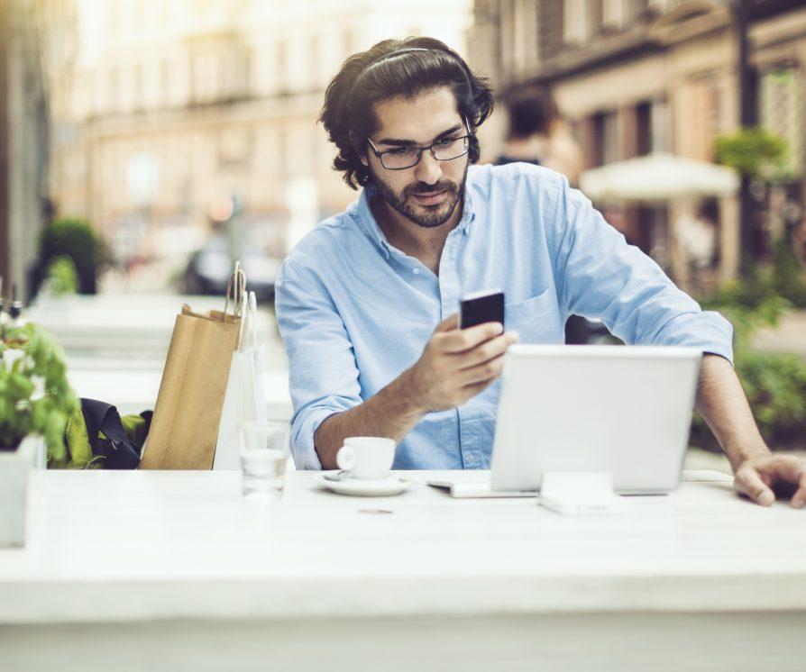 A virtual assistant sitting in a cafe working on a laptop with a coffee on the table.