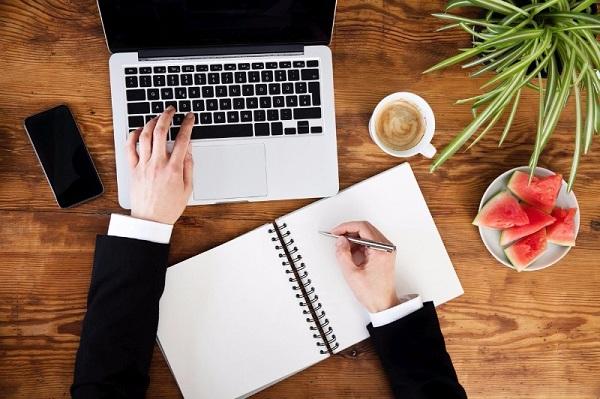 A man using a laptop and a notebook in a home office.