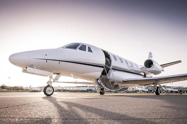 A small private plane on a tarmac with an open door. In the background, there’s a small airport.