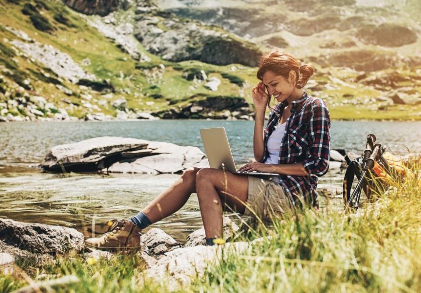 A woman working on a laptop at the side of a lake