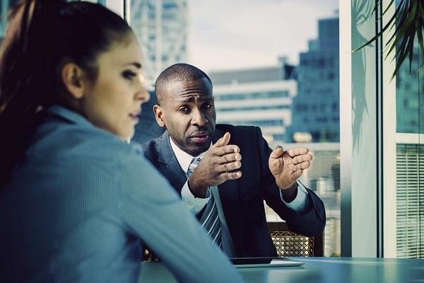A man talking to a colleague over a desk asking weird interview questions.