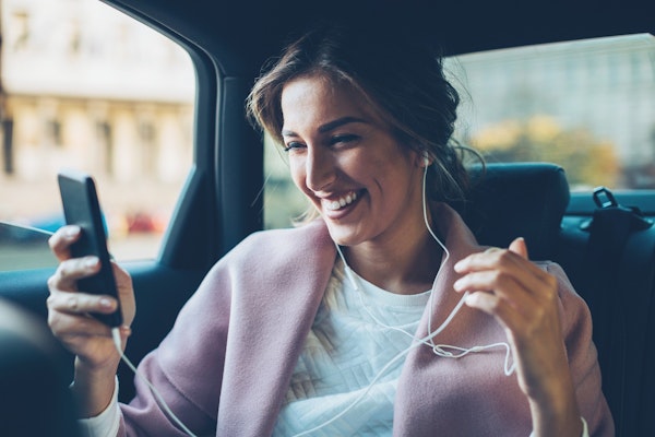 Woman in car with mobile in pink jacket holding her phone and smiling
