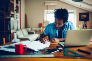Student at a desk at home with papers and a laptop