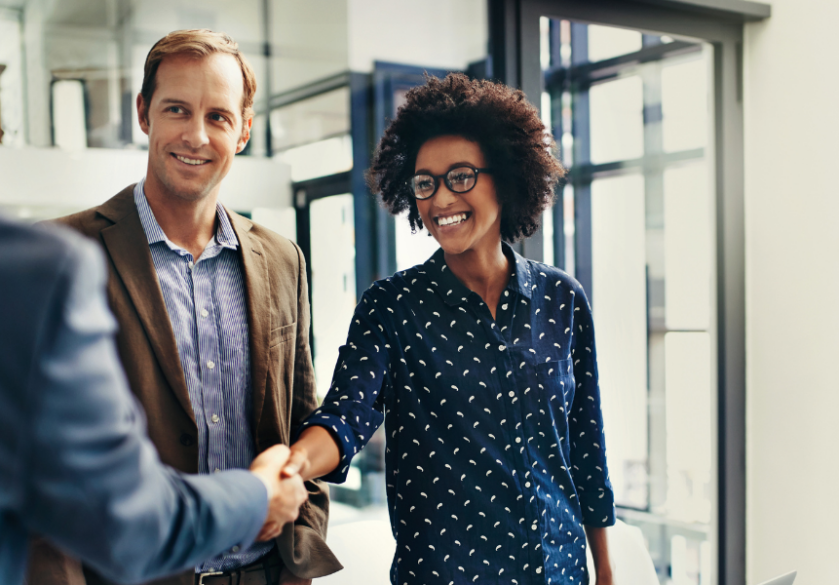 Three business people dressed in professional wear, two of them are shaking hands and smiling