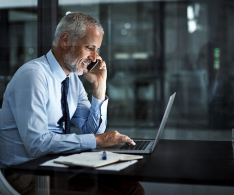 Man working on his laptop whilst on the phone in a dark office