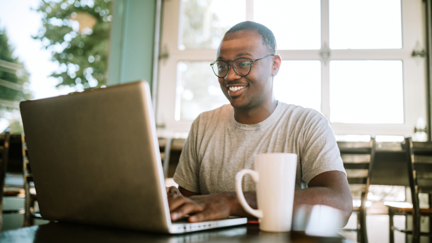 A man smiling at his laptop screen as he works remotely from home.